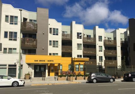 A modern four-story apartment building with balconies and a yellow entrance labeled 