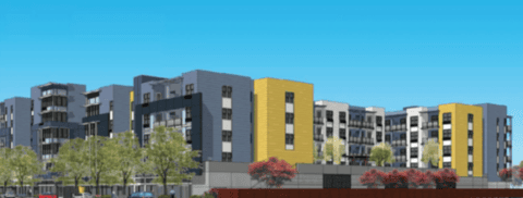 A modern multi-story apartment complex with gray, white, and yellow panels, surrounded by trees and landscaping under a clear blue sky.